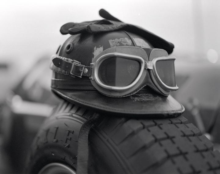 A vintage leather helmet with goggles and gloves rests on a tire.