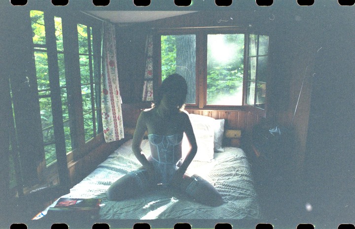 A woman in lingerie kneels on a bed in a cabin with sunlight streaming through the windows.