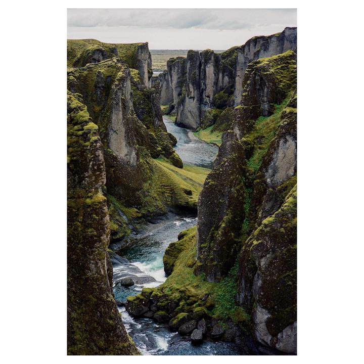 A river flows through a deep canyon with steep, moss-covered rock walls under a cloudy sky.