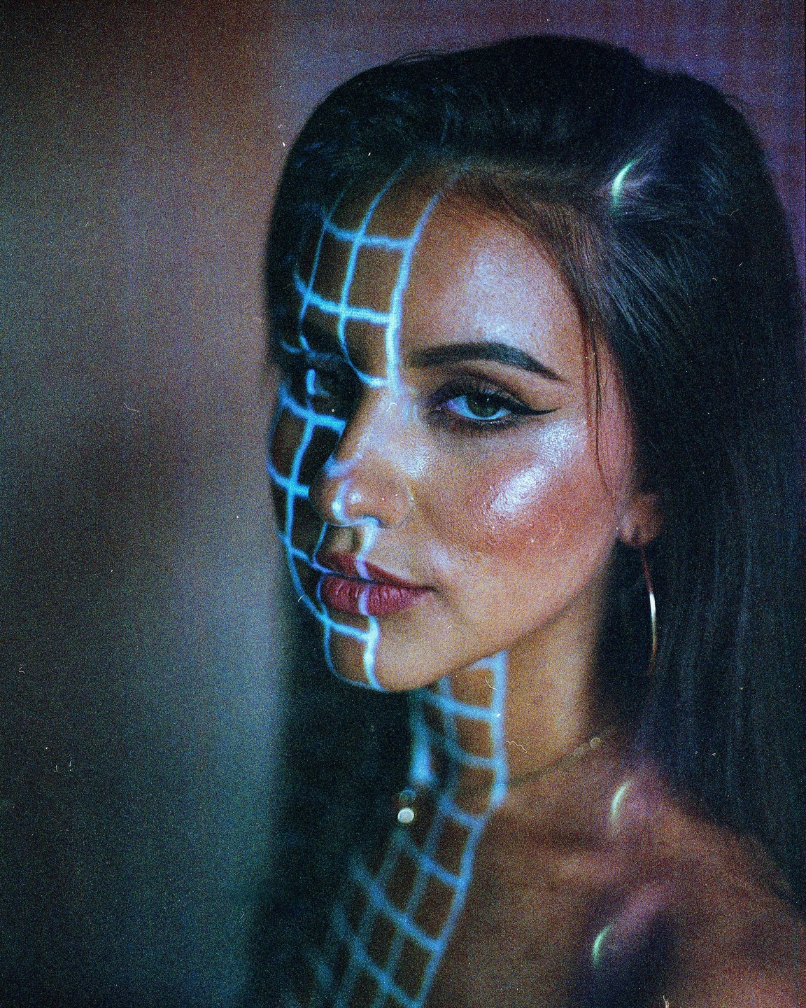 A woman with long dark hair has a grid pattern projected onto her face and neck.