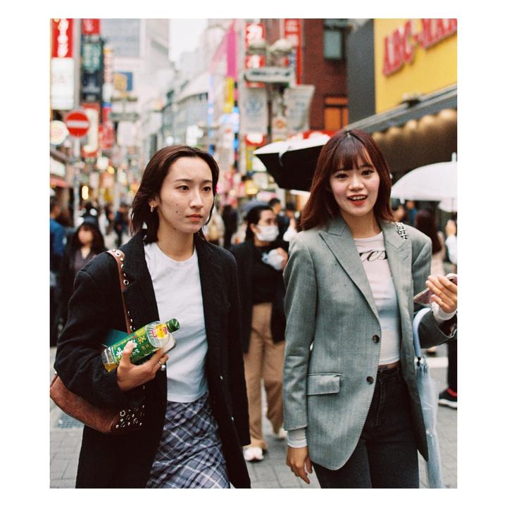 Two women walk down a busy street lined with shops and signs.