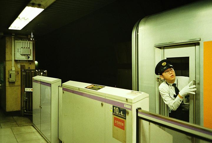 A man in a uniform and hat looks out from a train door at a station platform at night.