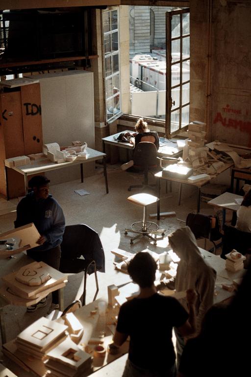 Students work on models in a sunlit studio with an open window overlooking a construction site.