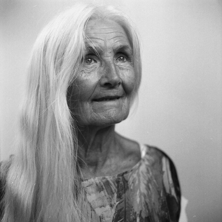 A woman with long white hair looks up and smiles.