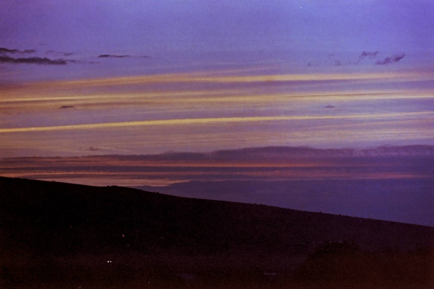 The sky is filled with colorful clouds above a dark hillside at sunset.