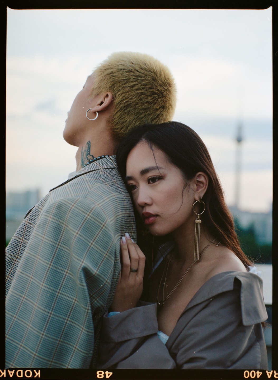 A woman rests her head on a man's shoulder, both looking away from the camera.