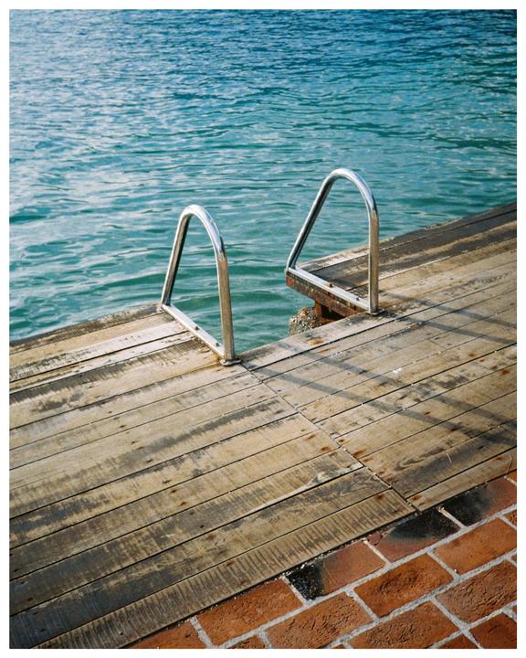 A metal ladder extends from a wooden dock into the blue water next to a brick path.