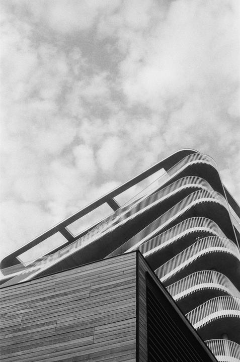 A low-angle view shows a modern building with curved balconies and a section clad in wood.
