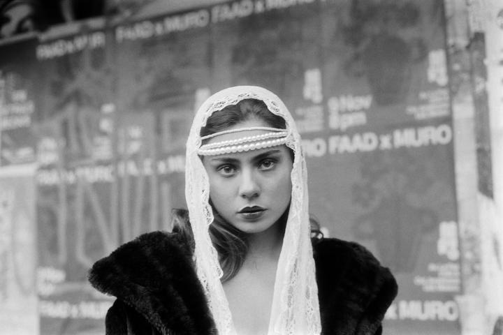 A woman wearing a lace veil and pearls looks directly at the viewer.