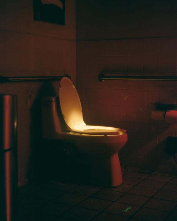 A toilet with its lid open is illuminated by a warm glow in a dimly lit bathroom.