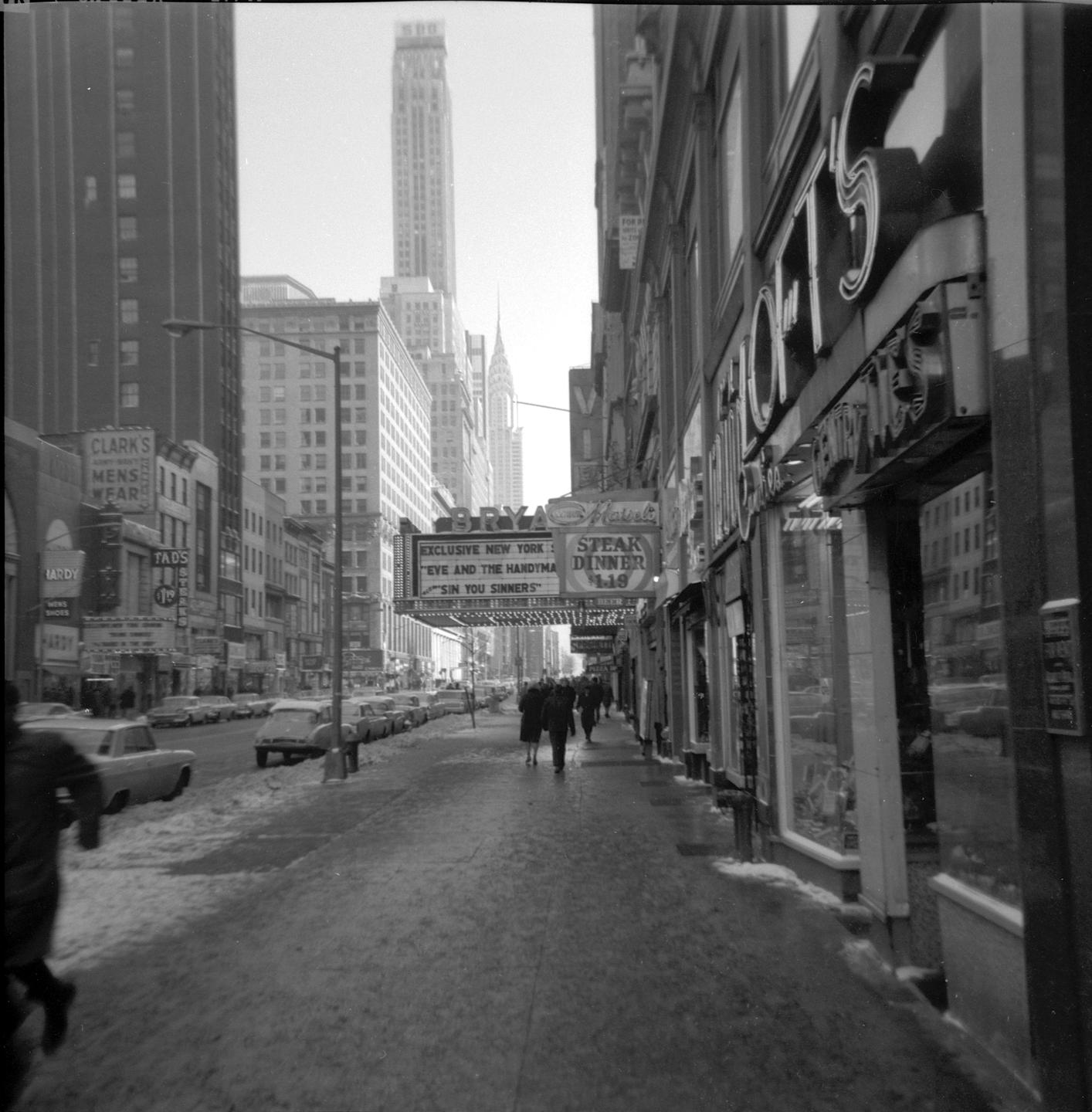A street in New York City is covered in snow with people walking on the sidewalk and cars parked along the curb.
