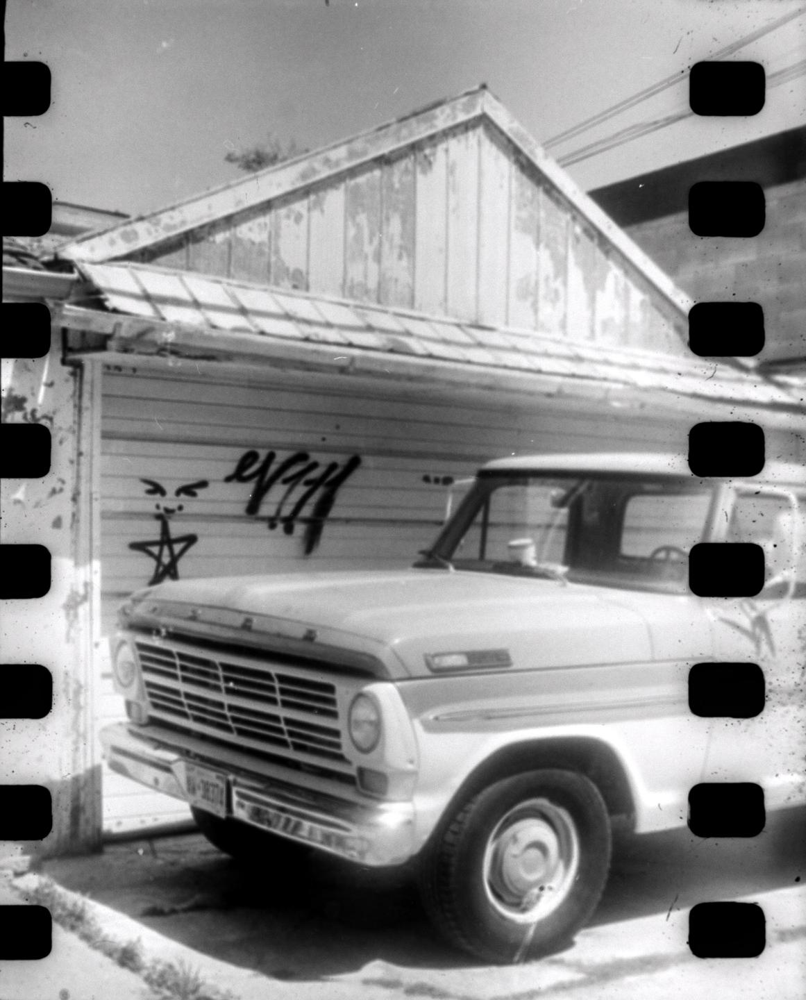A vintage truck is parked in front of a building with peeling paint and graffiti.