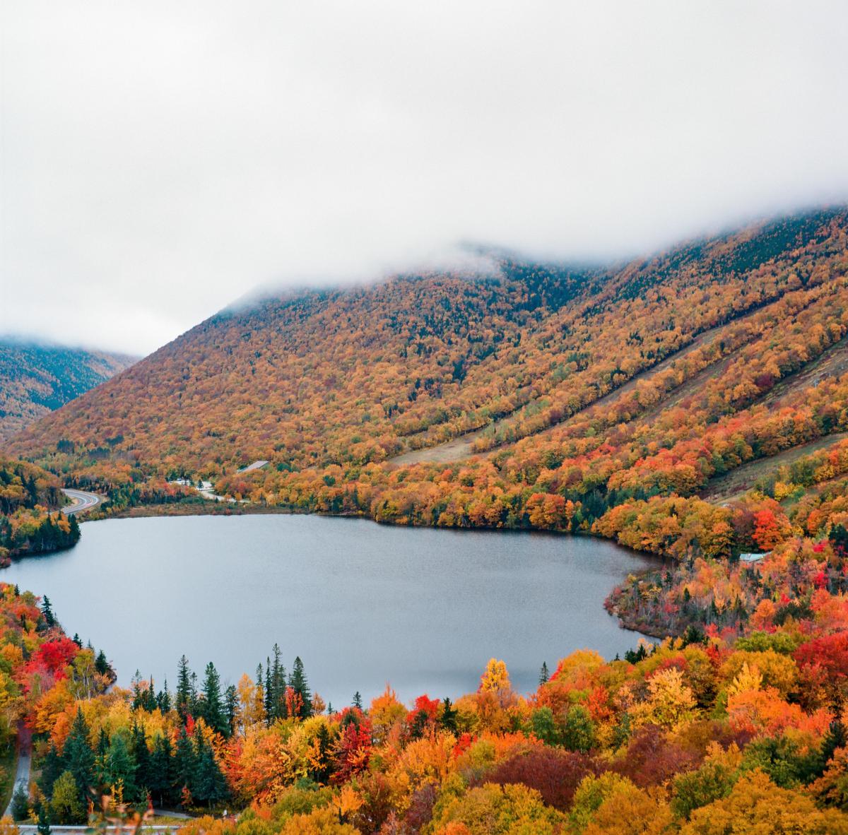 A lake is surrounded by mountains covered in autumn foliage under a cloudy sky.
