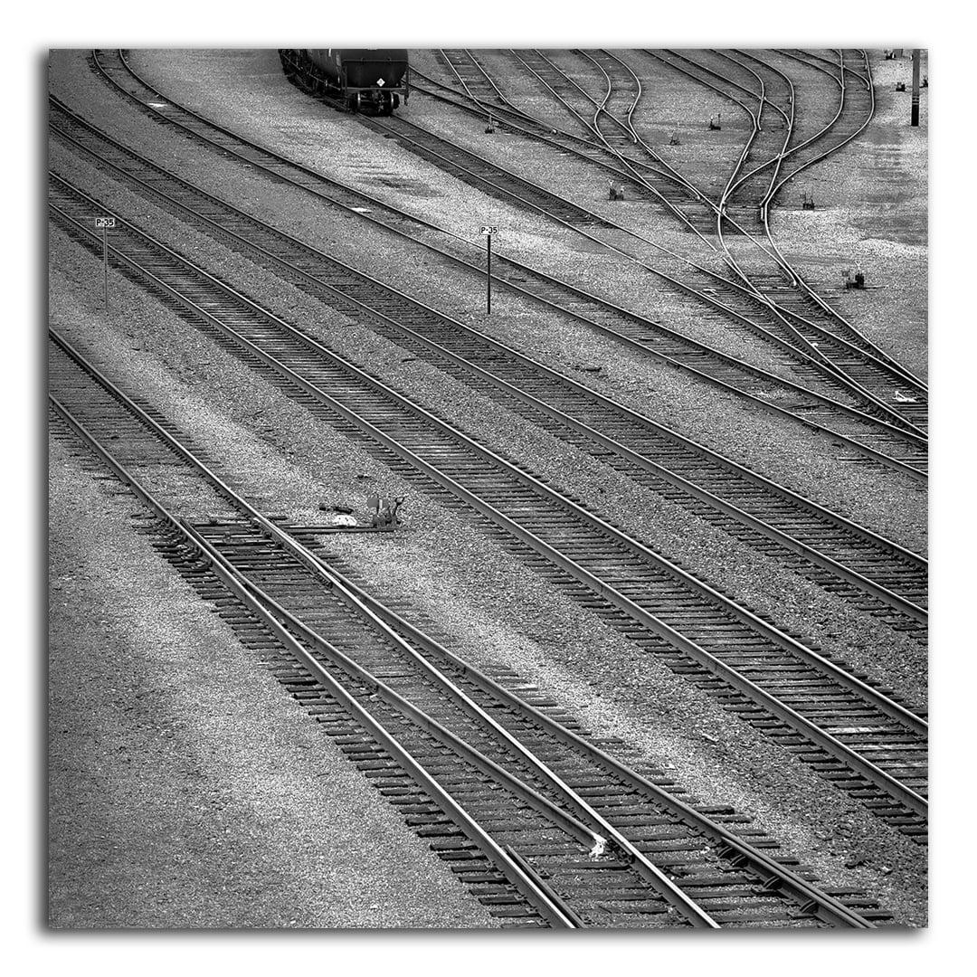 Multiple train tracks converge and diverge in a rail yard with a train car visible in the distance.