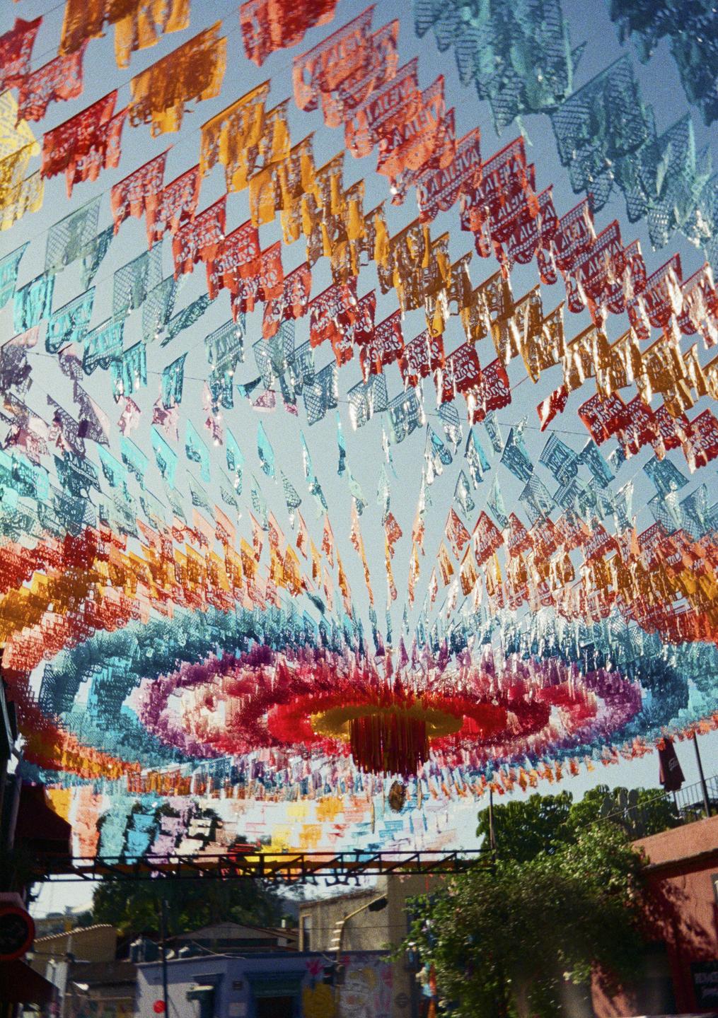 Colorful papel picado banners are strung across a street, creating a vibrant canopy.