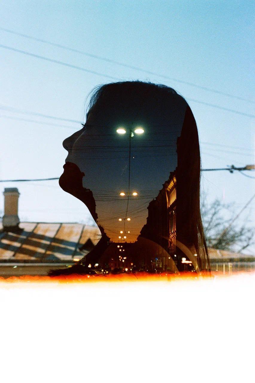 A double exposure shows the silhouette of a woman's head overlaid with a street scene at dusk.