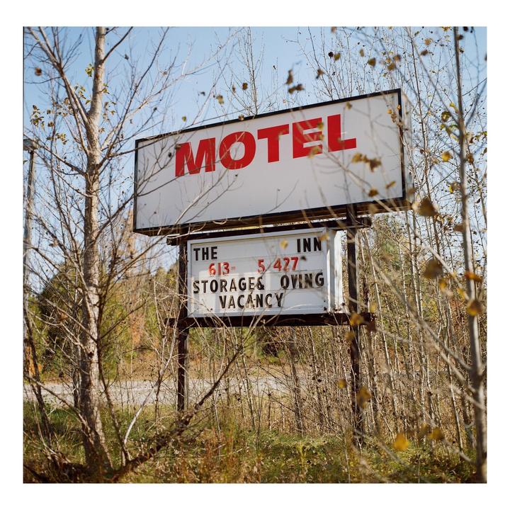 A motel sign with red lettering stands among bare trees and dry brush.