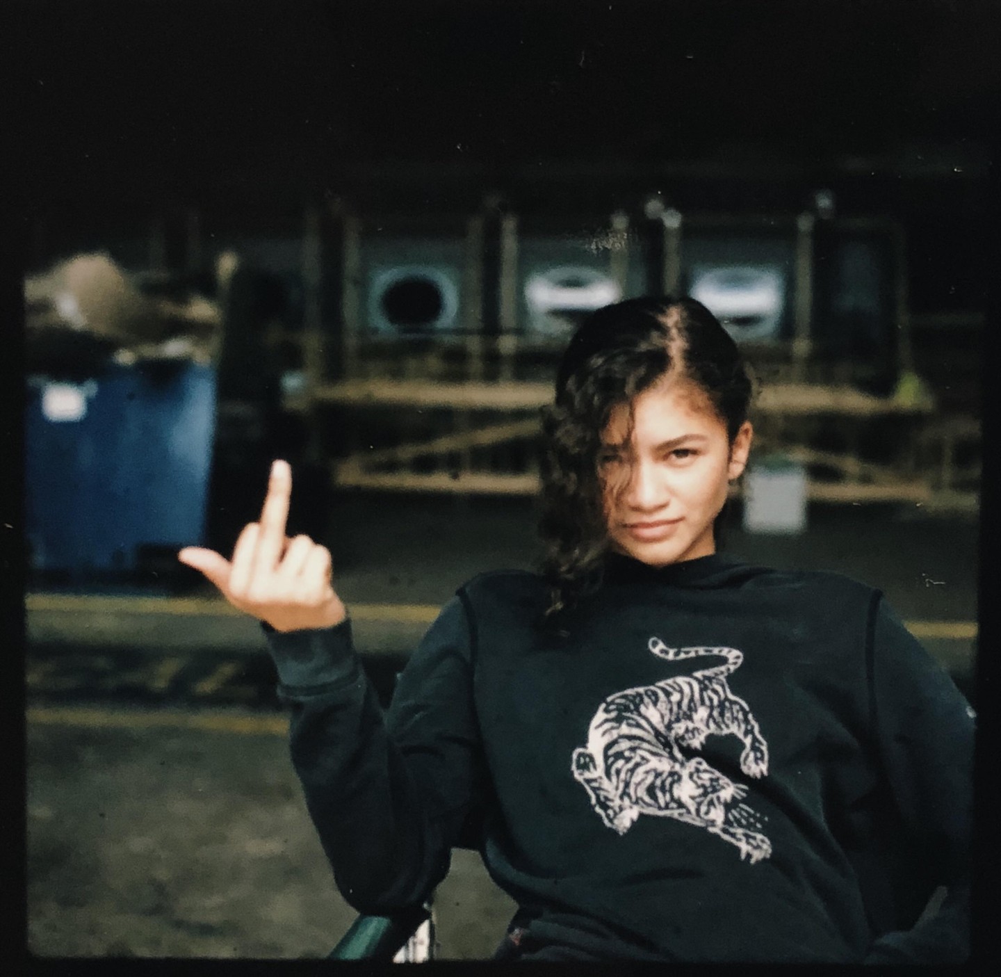 A woman in a dark sweatshirt with a tiger design sits and gives the middle finger.