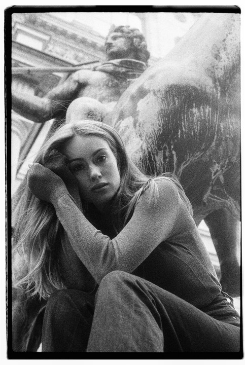 A woman with long hair sits in front of a statue of a man on a horse.