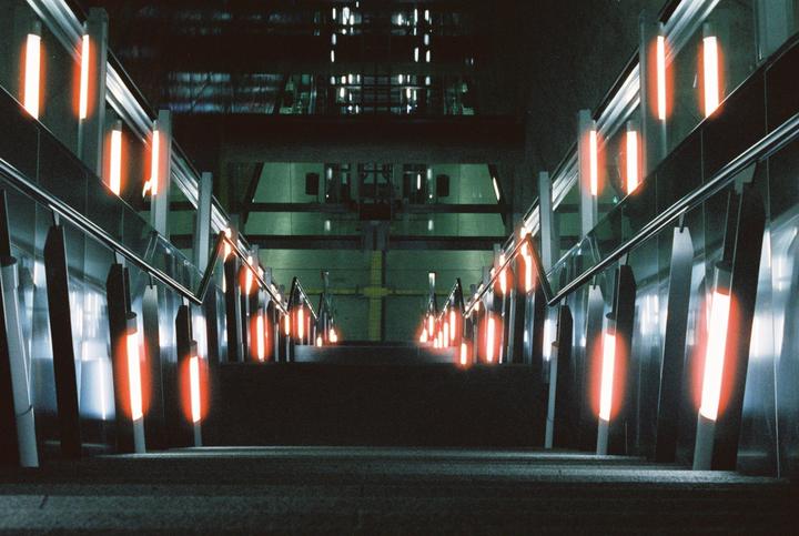 An escalator with orange lights descends into a dark subway station.