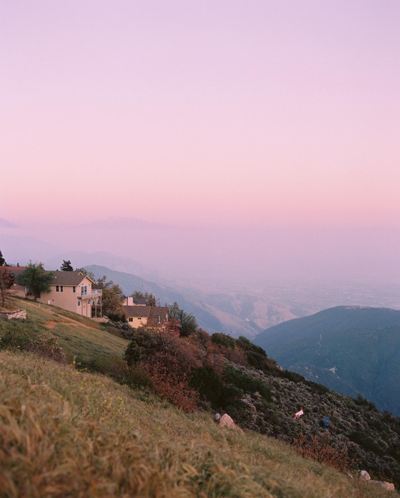 Houses are nestled on a hillside overlooking a valley at sunset.