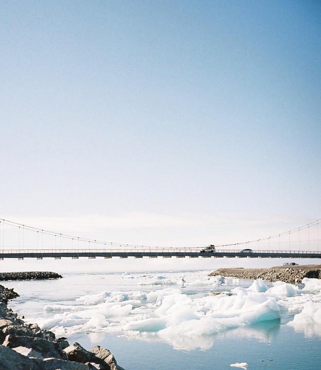 A bridge spans a body of water filled with icebergs, with a vehicle driving across the bridge.