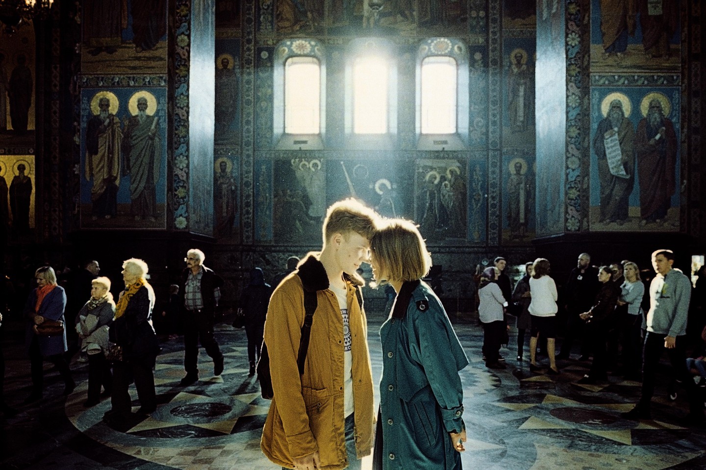 A couple stands forehead to forehead in a church with painted walls and bright windows.