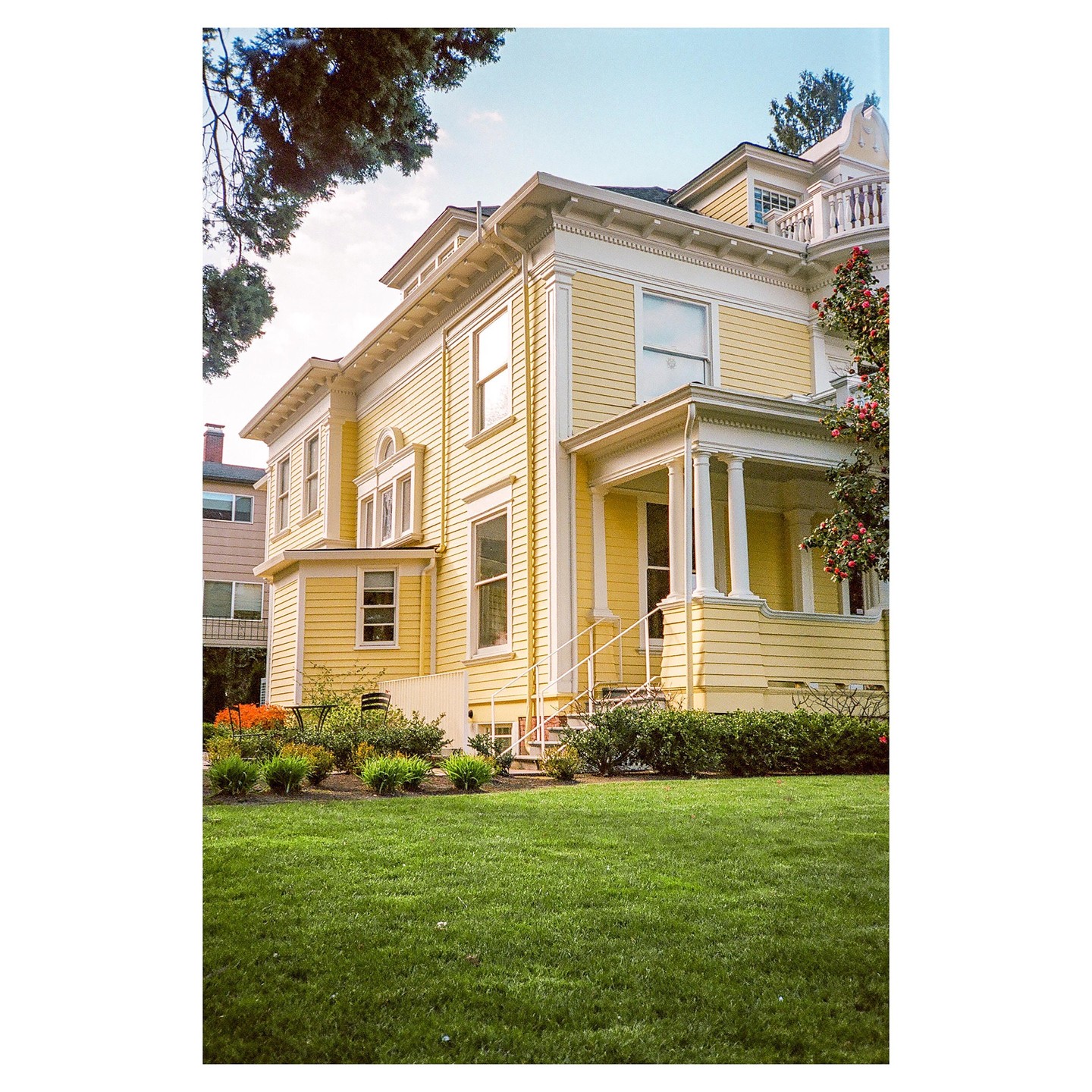 A large yellow house with white trim and a green lawn is seen from a low angle.