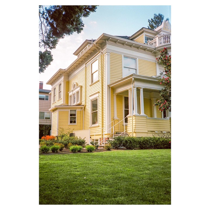 A large yellow house with white trim and a green lawn is seen from a low angle.