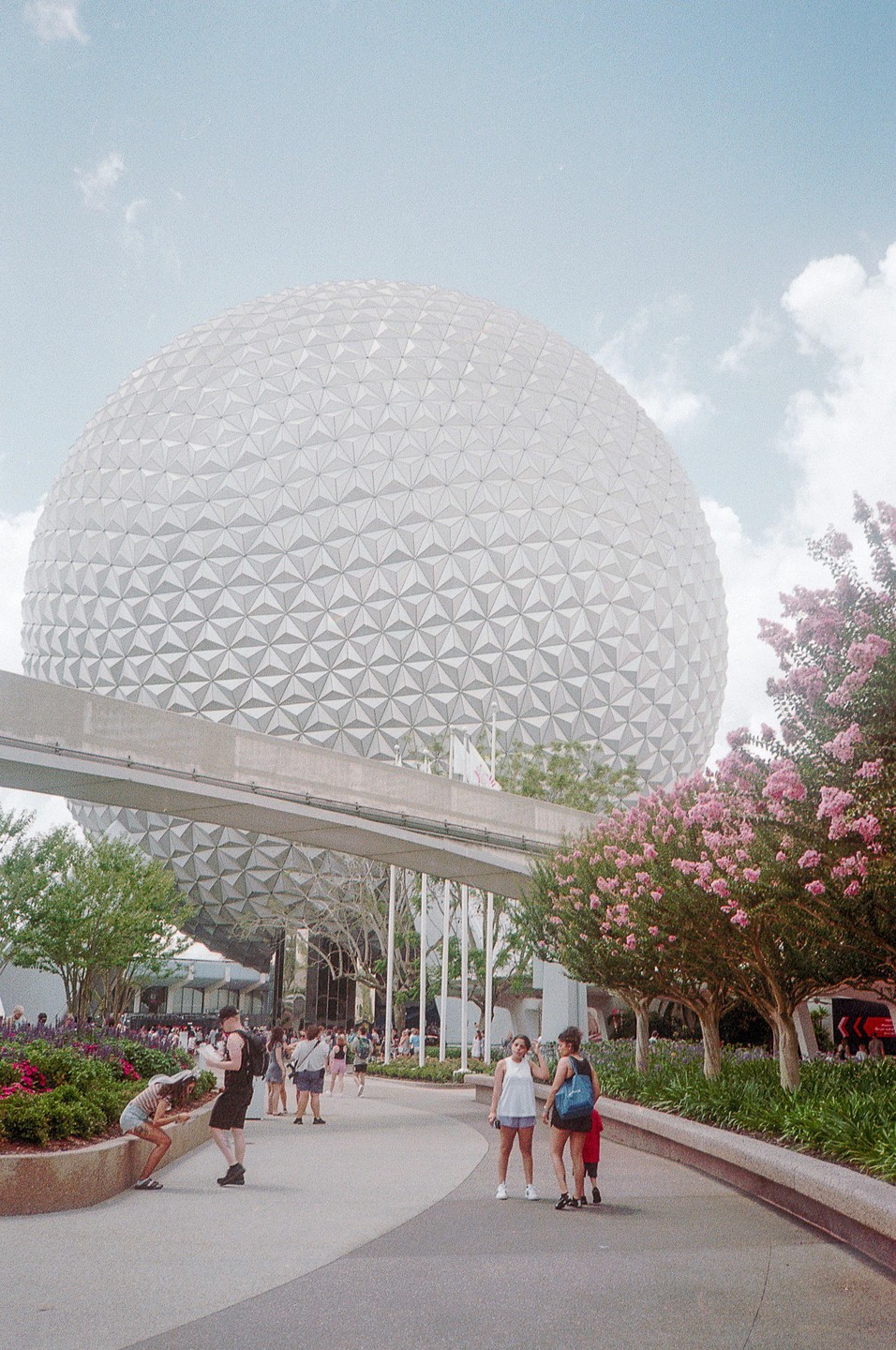A large geodesic dome stands over a path with people walking and flowering trees.