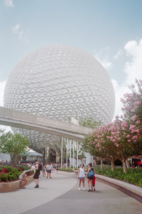 A large geodesic dome stands over a path with people walking and flowering trees.