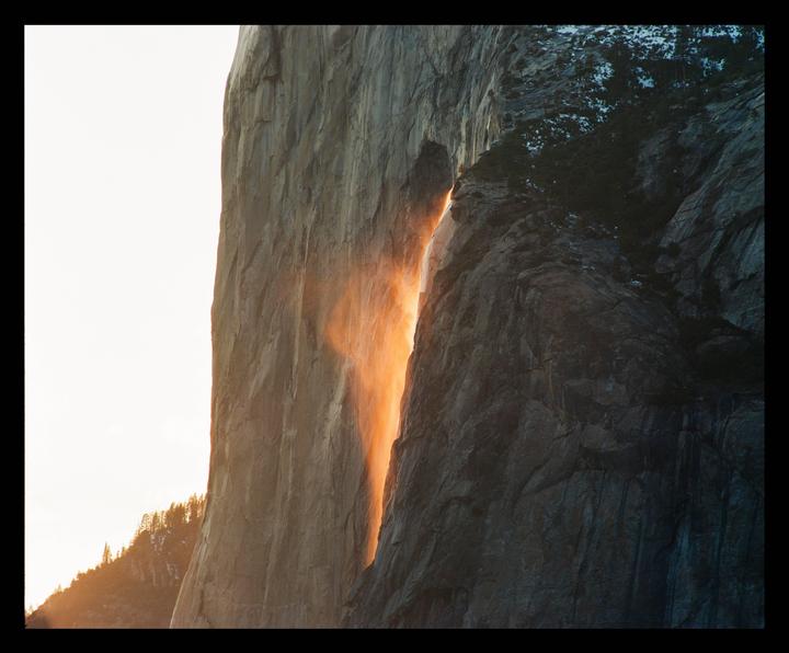 A waterfall glows orange between two large rock formations at sunset.
