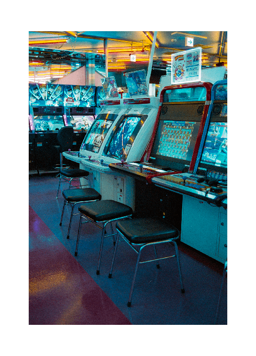 An arcade with multiple video game machines and stools is illuminated by neon lights.