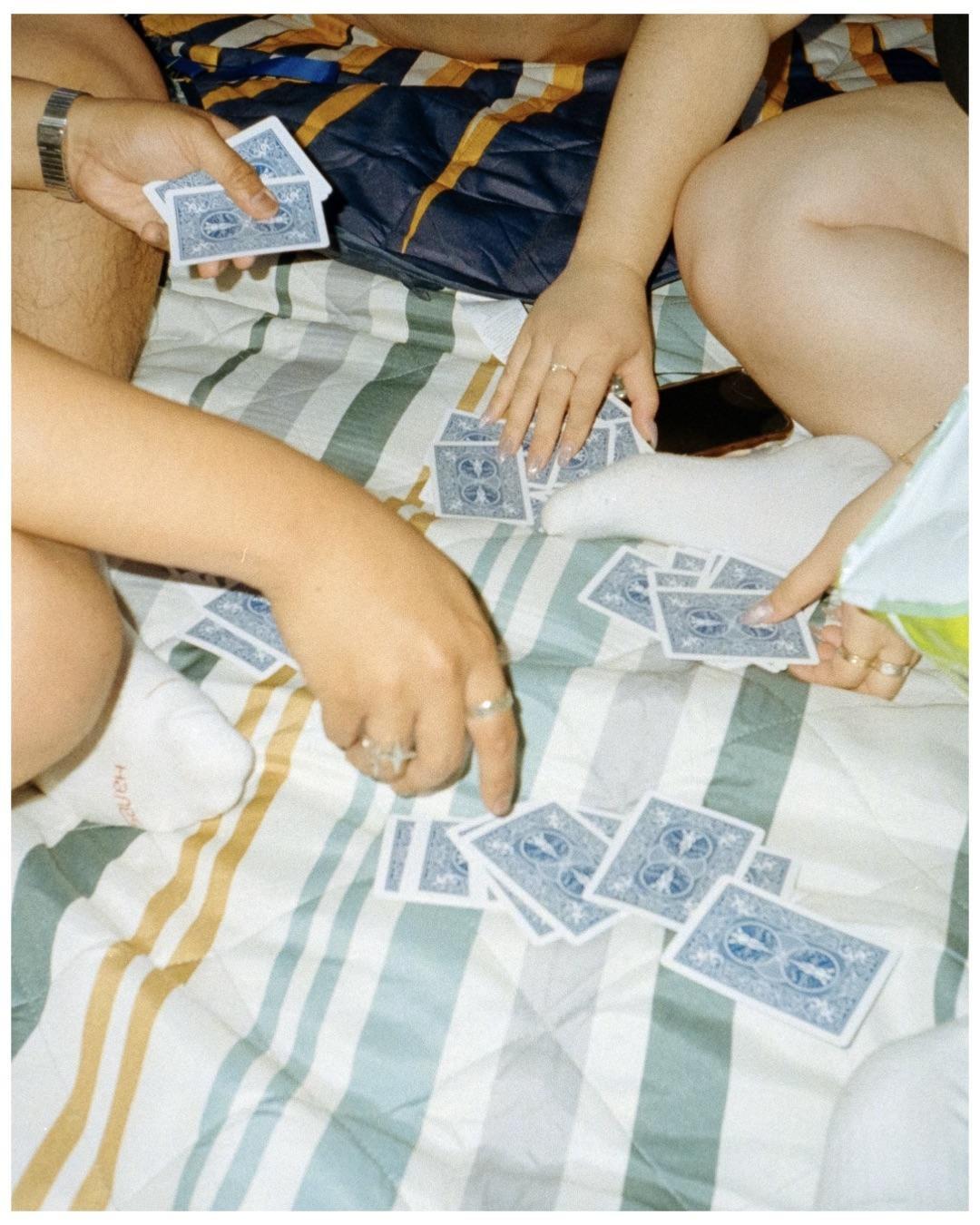 Three people play cards on a striped blanket.