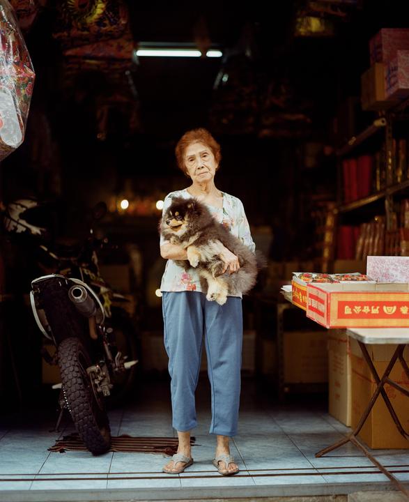 A woman stands in a doorway holding a fluffy dog, with a motorcycle and boxes visible in the background.
