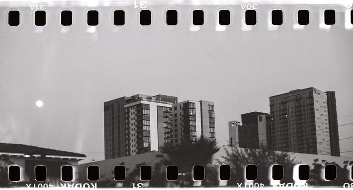 A bright moon hangs in the sky above several buildings and trees.