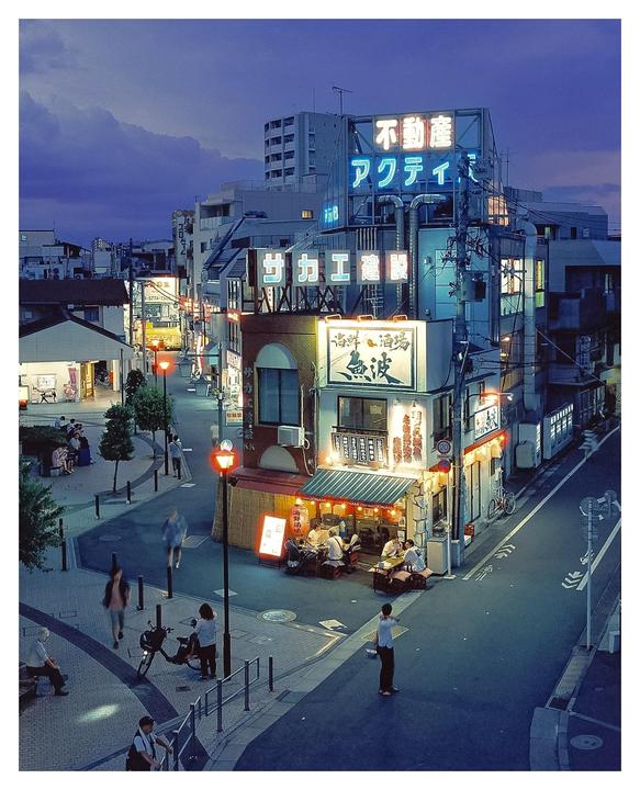 A street corner in a city is illuminated by neon signs and streetlights at dusk.