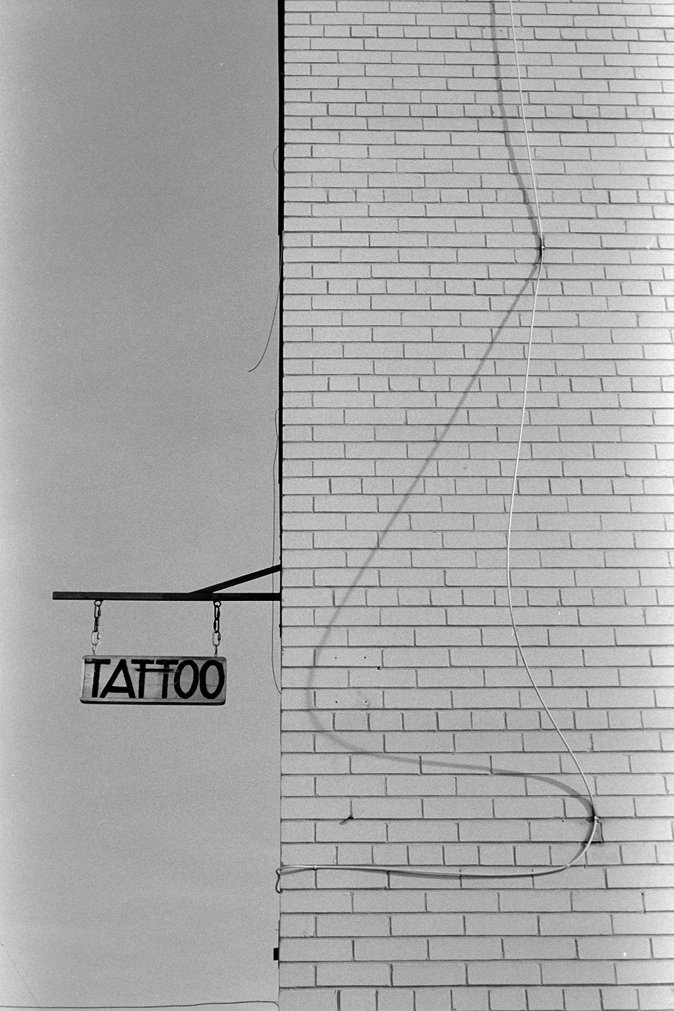 A tattoo sign hangs from a brick building under a clear sky.