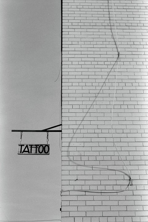 A tattoo sign hangs from a brick building under a clear sky.