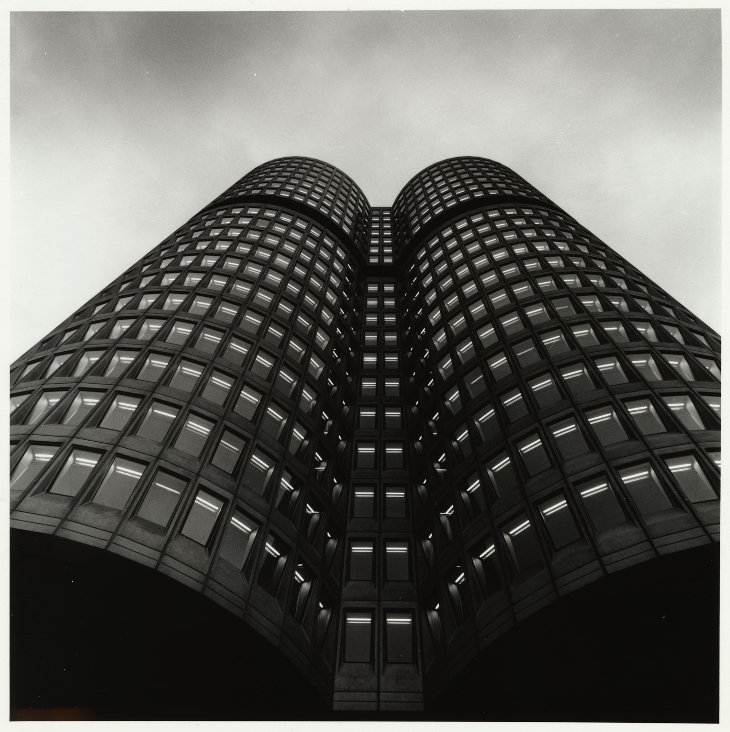 A low-angle, black and white shot of a tall, modern building with many windows, some of which are lit.