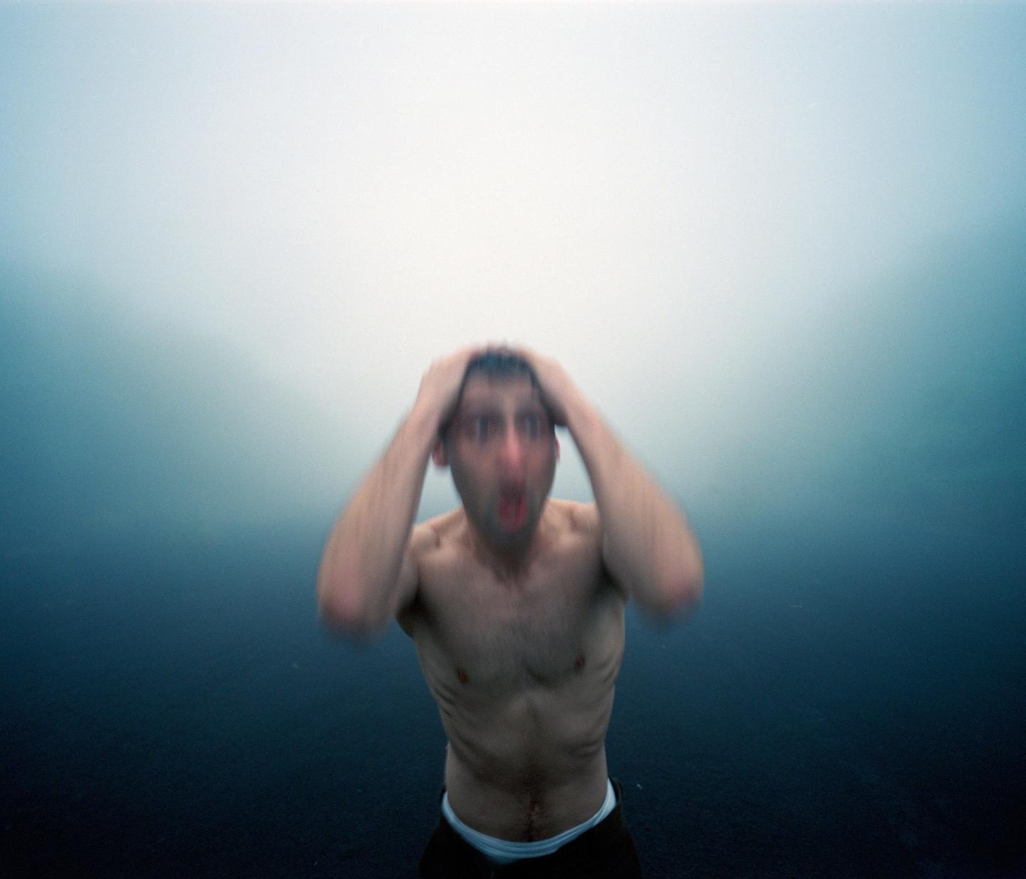 A man with his hands on his head and his mouth open appears to be screaming underwater.