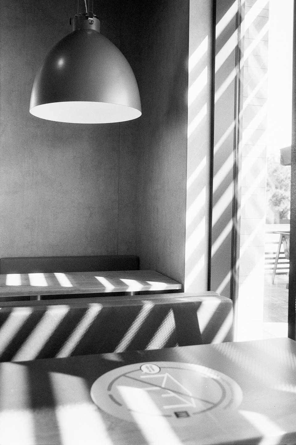 Sunlight streams through a window, casting striped shadows across a booth and table in a cafe.