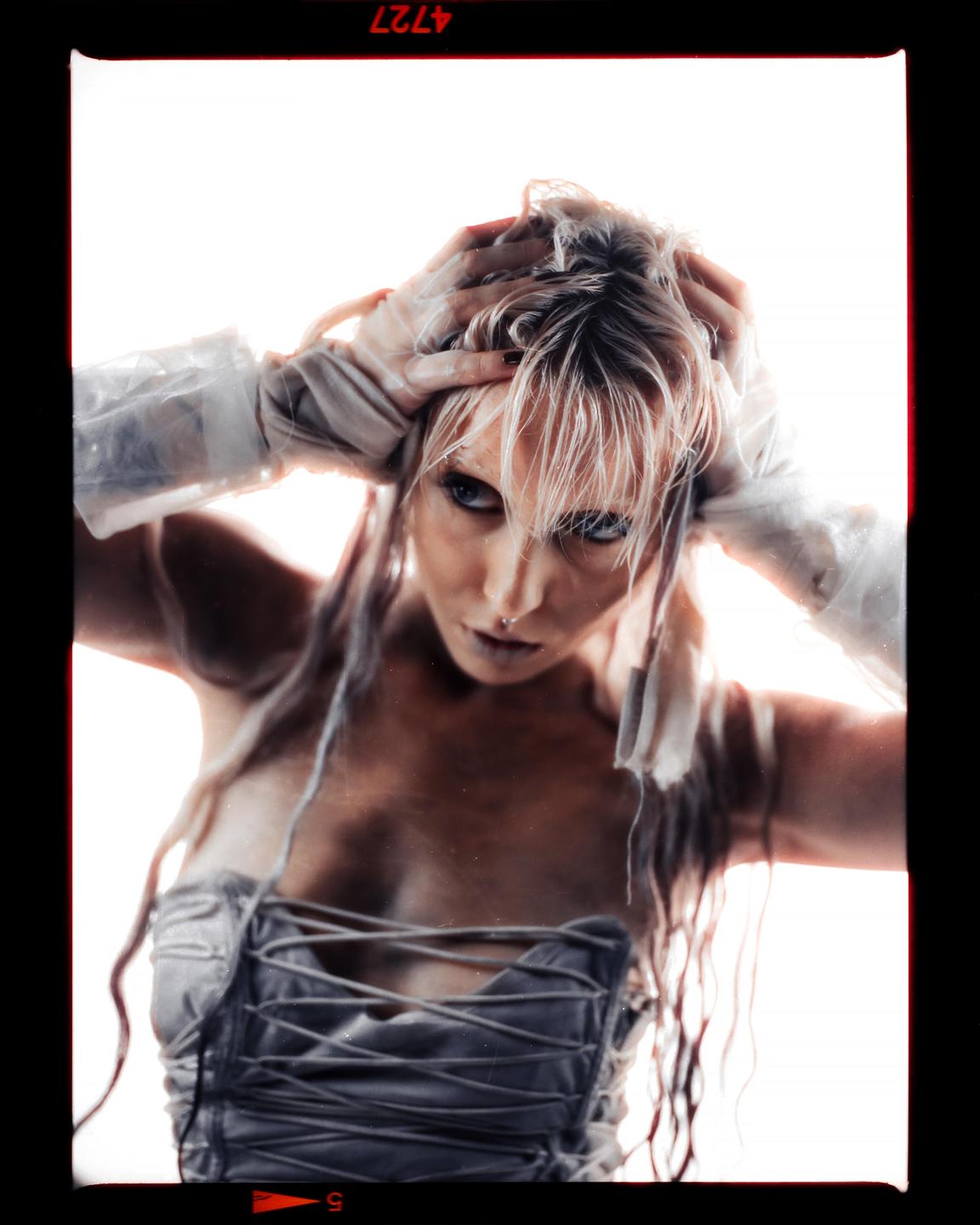 A woman with wet hair and a corset looks directly at the viewer.
