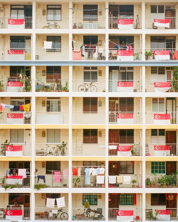 A grid of balconies on a housing complex is adorned with many Singaporean flags and laundry.