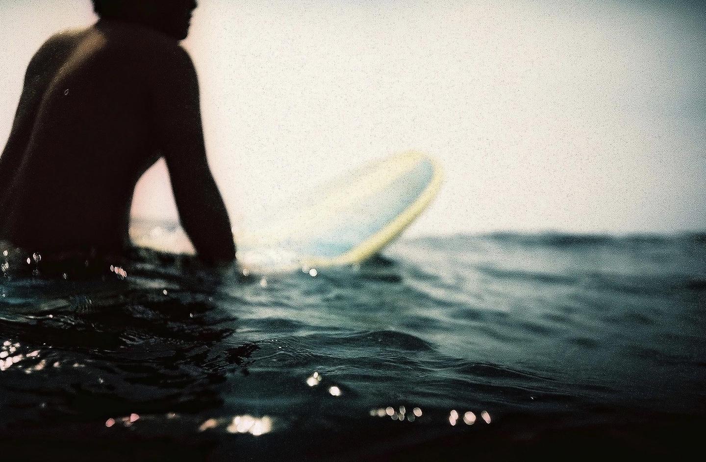 A surfer sits on a surfboard in the ocean, with the water rippling around them.