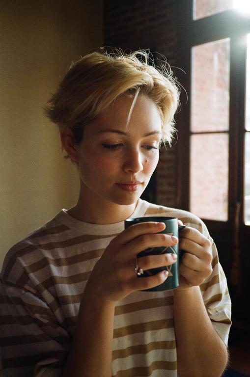 A woman with short blonde hair holds a mug with both hands, looking down at it.