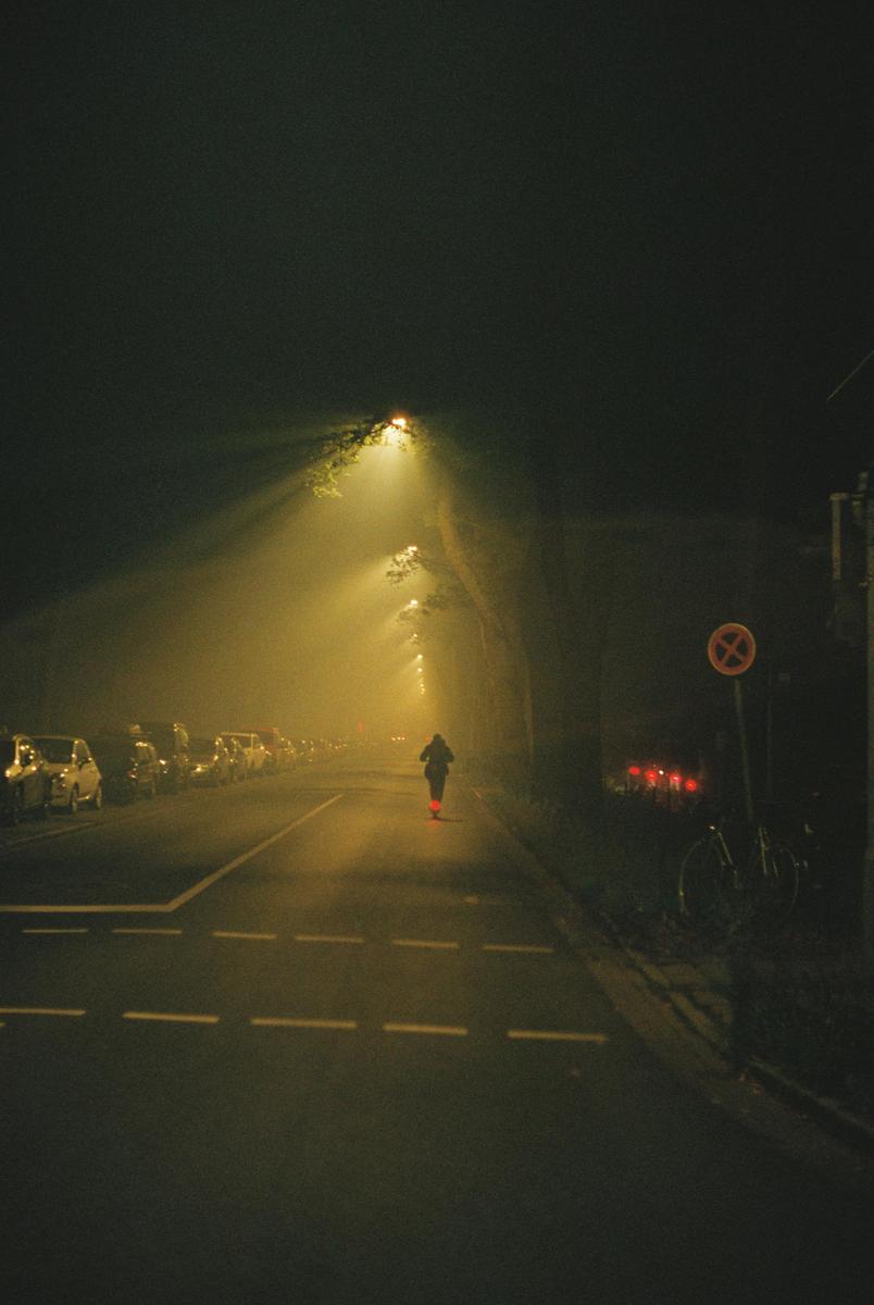 A person walks down a street at night, illuminated by streetlights and car headlights.