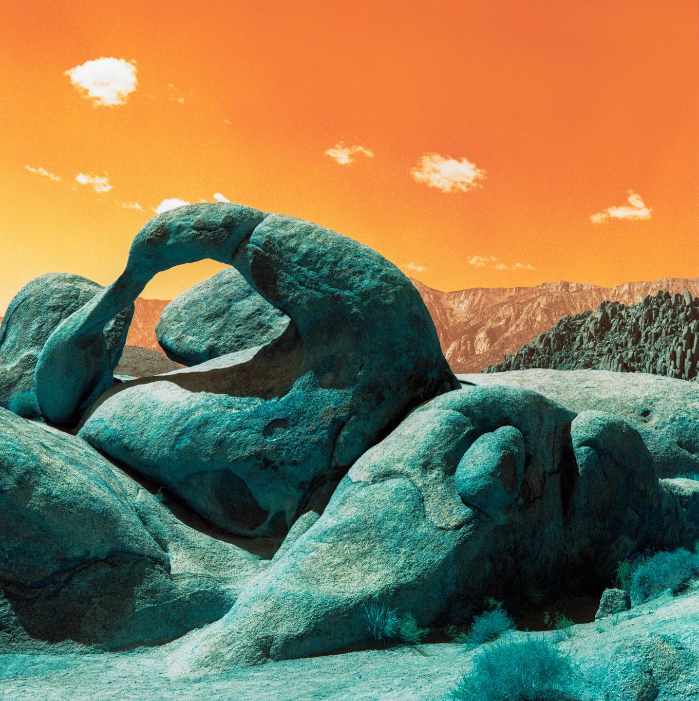 A rock formation with an arch is visible under an orange sky with small clouds.