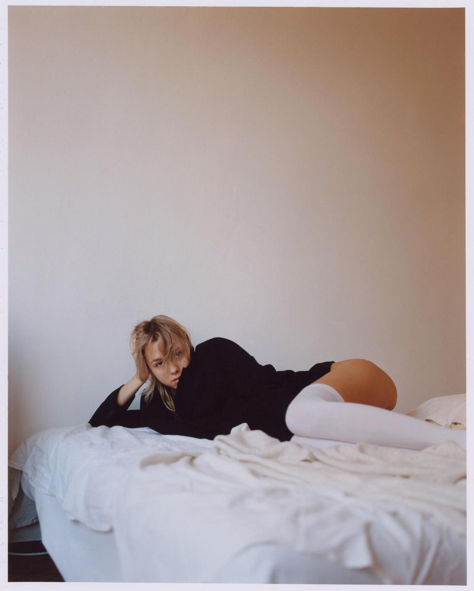 A woman in a black shirt and white thigh-high socks is lying on a bed.