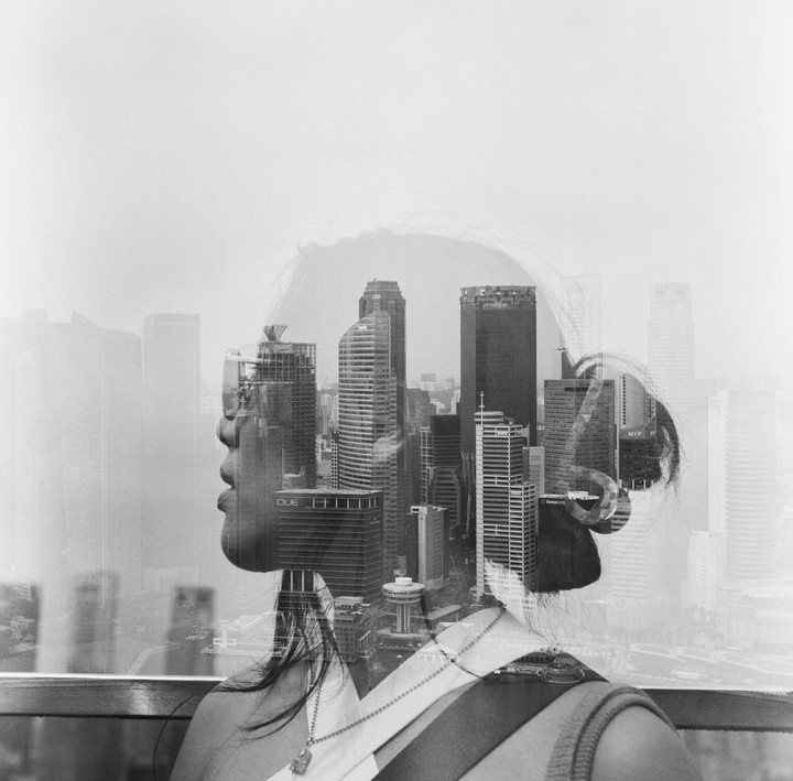 A woman's profile is double exposed with a cityscape of tall buildings.
